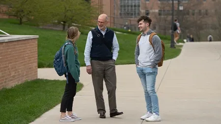 Professor talking with a male and female student on sidewalk outside